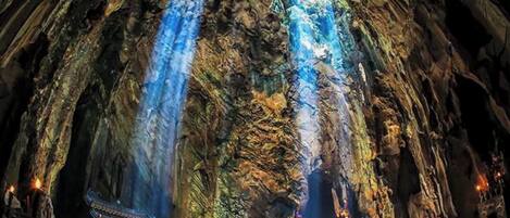 A cave with a waterfall and a small temple at the bottom.