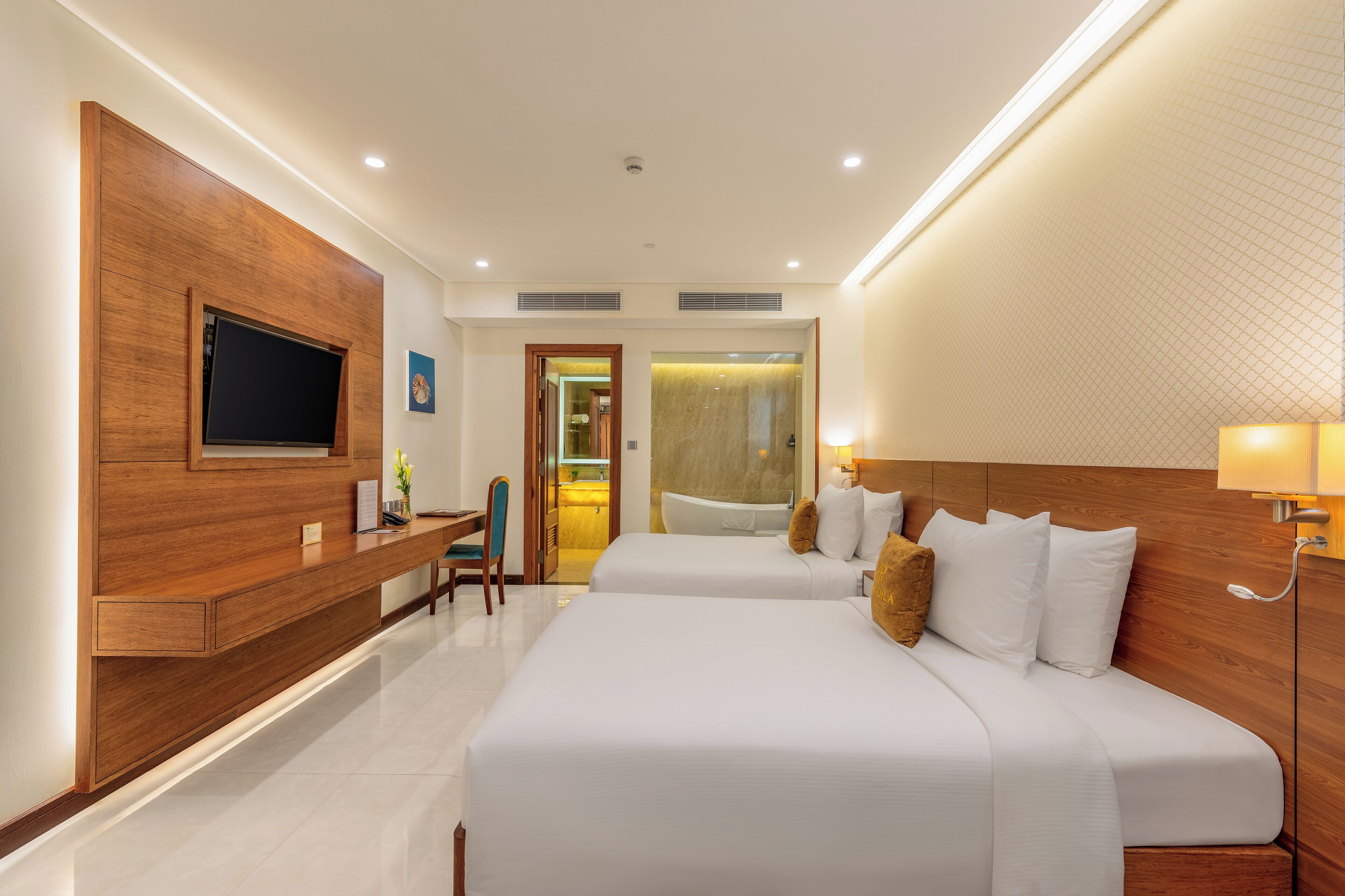 A hotel room with two beds, a desk, a TV, and a bathroom visible through an open door.
