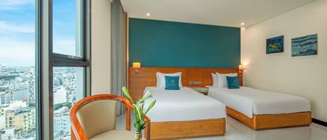 A hotel room with a city view, two beds, a wooden headboard, a round table with fruit, and a chair.