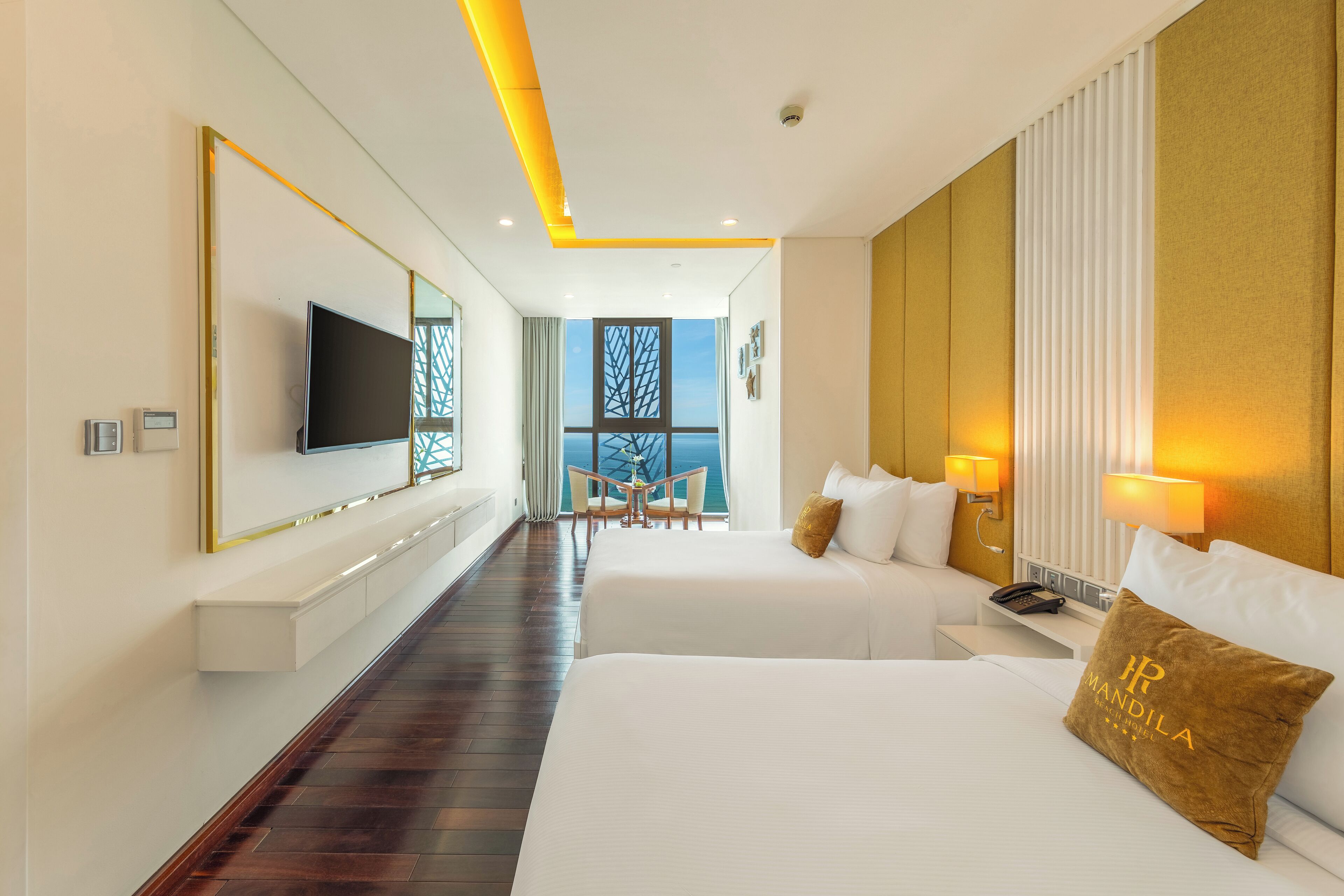 Habitación de hotel con dos camas, televisión, escritorio y vista al mar.
