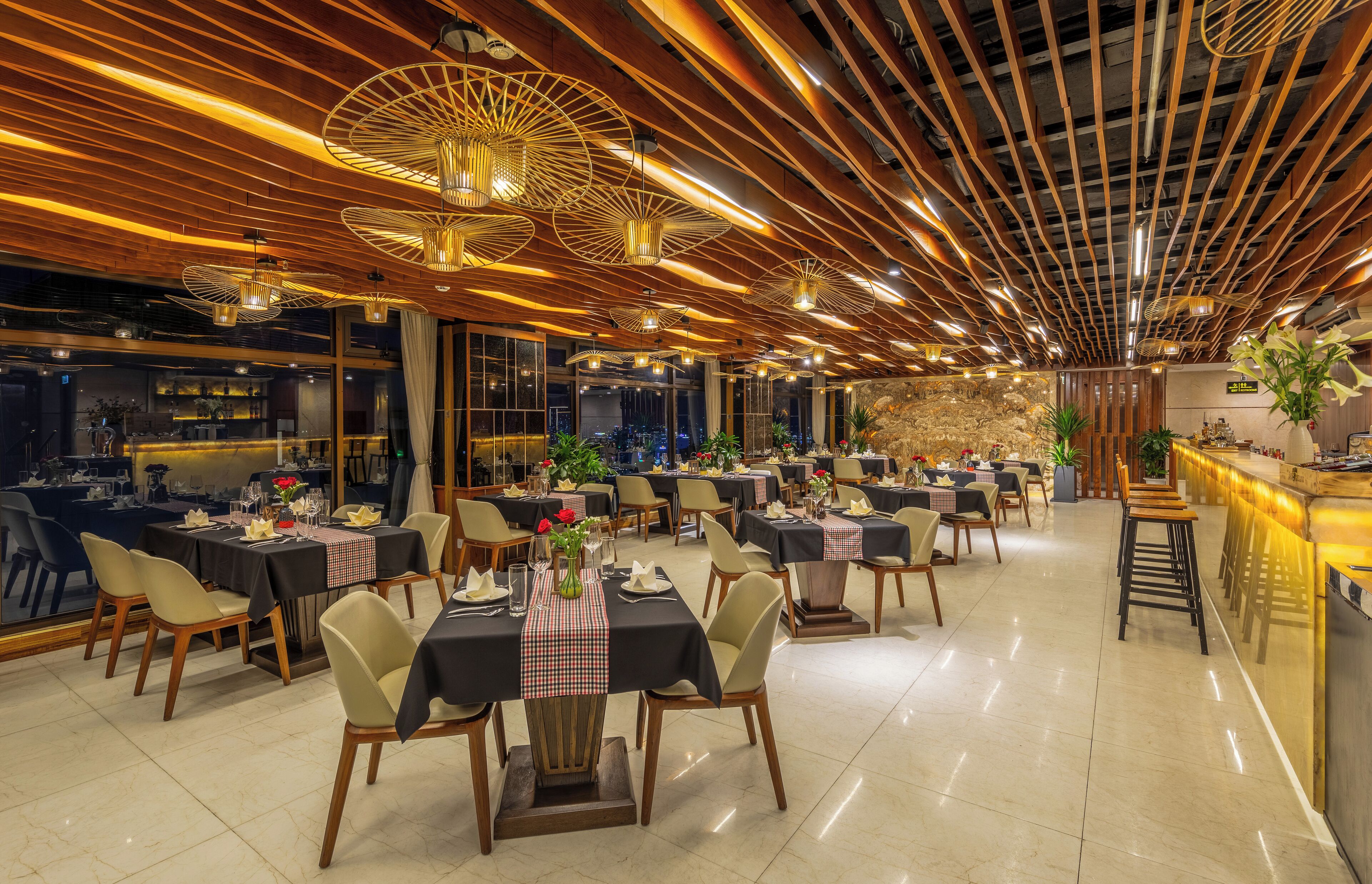 A spacious restaurant with multiple dining tables, wooden ceiling design, and ambient lighting.