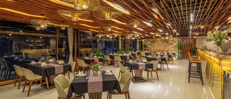 A spacious restaurant with multiple dining tables, wooden ceiling design, and ambient lighting.