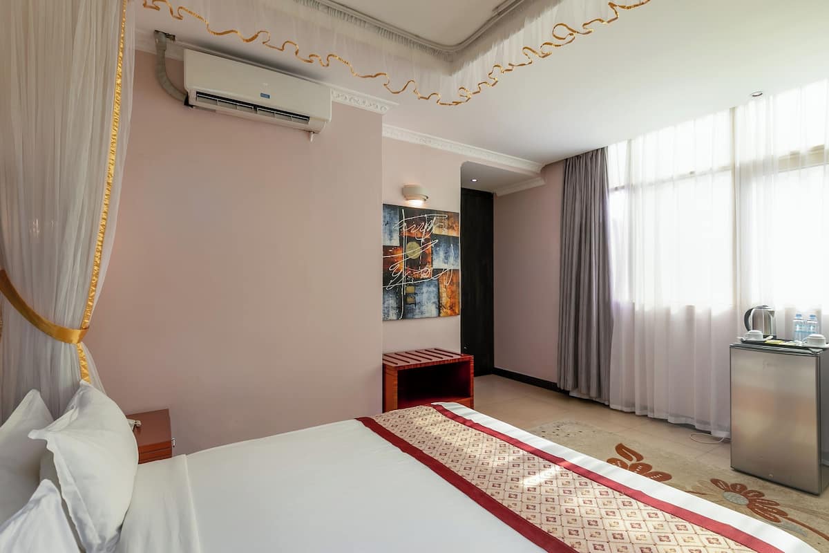 Habitación de hotel con cama, unidad de aire acondicionado, obra de arte, una mesita pequeña y un escritorio con tetera.