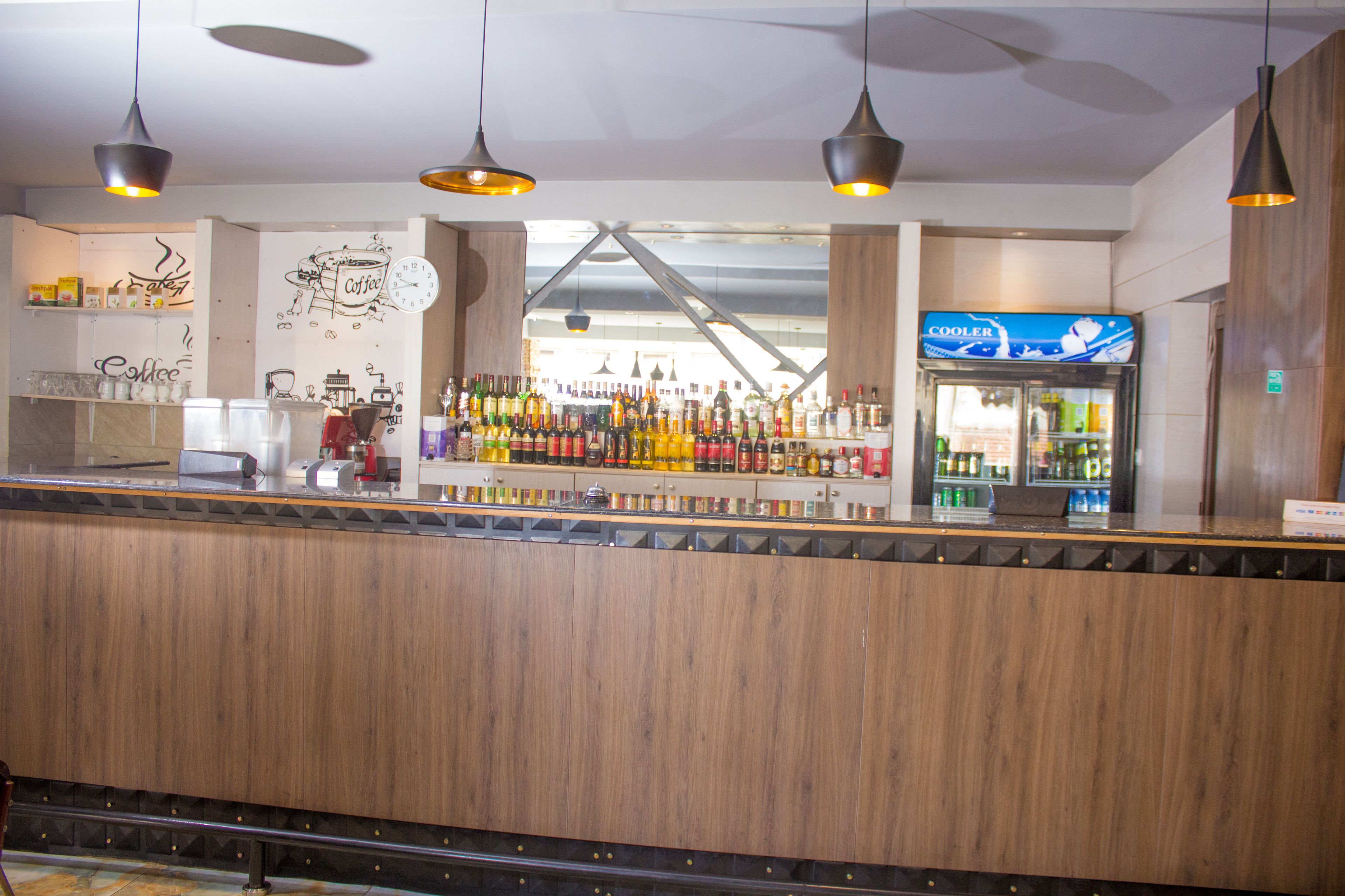 Zona de bar con mostrador de madera, lámparas colgantes y un letrero de nevera.