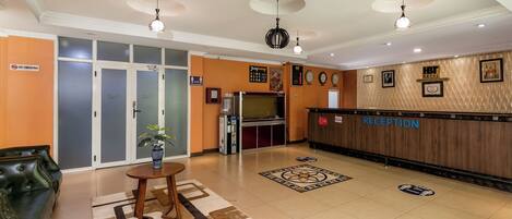 A hotel reception area with a reception desk, a seating area with a sofa, a coffee table, and a patterned rug.