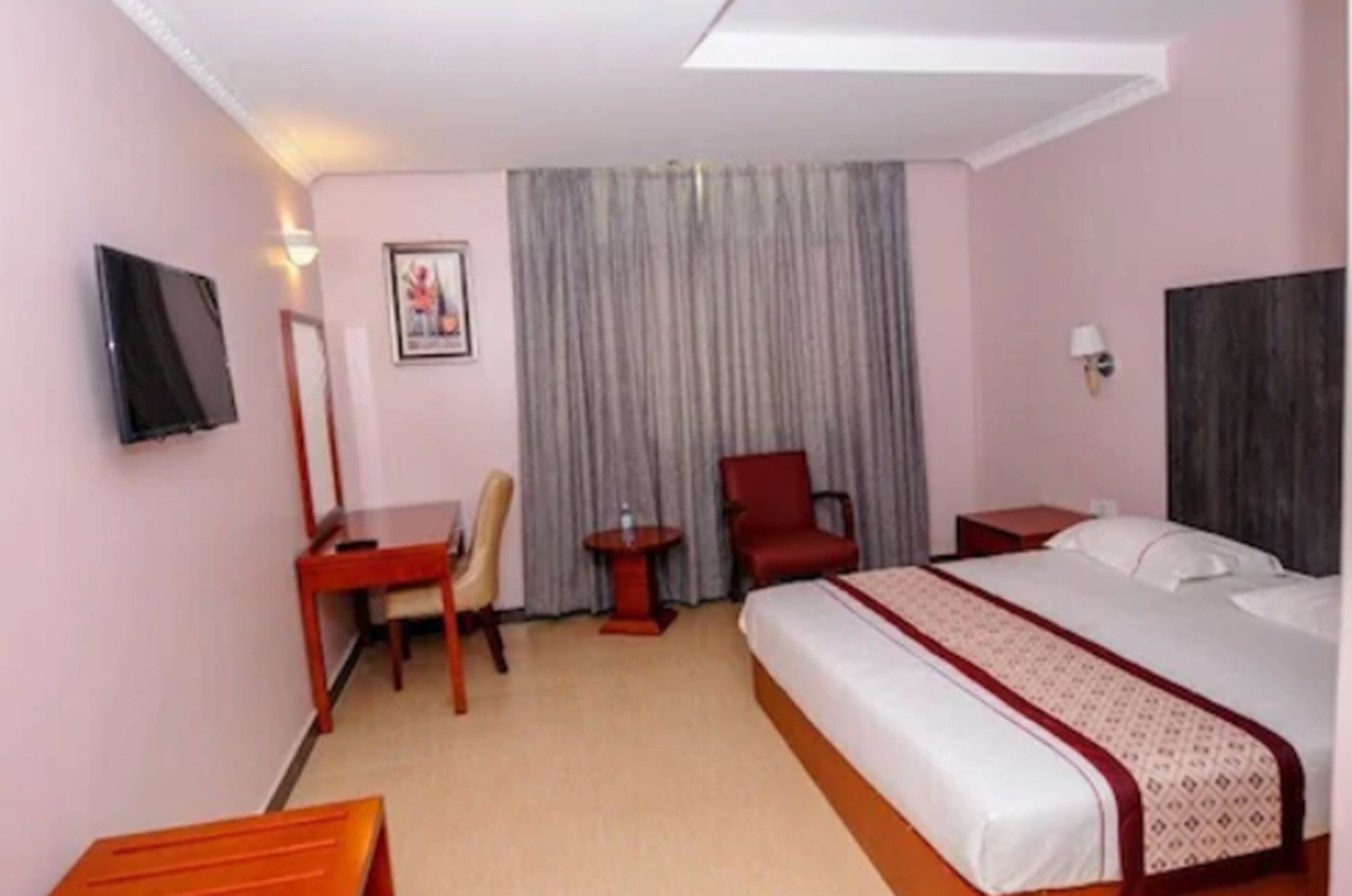 A hotel room with a bed, a desk, a chair, a TV, and a curtain.