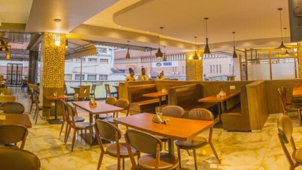 A restaurant with booths and tables, a patterned column, and hanging lights. - Russel Hotel (Kampala)