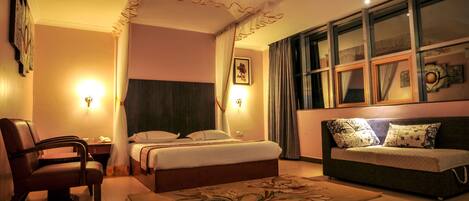 Une chambre d’hôtel avec un lit, un canapé, une chaise et une grande fenêtre.