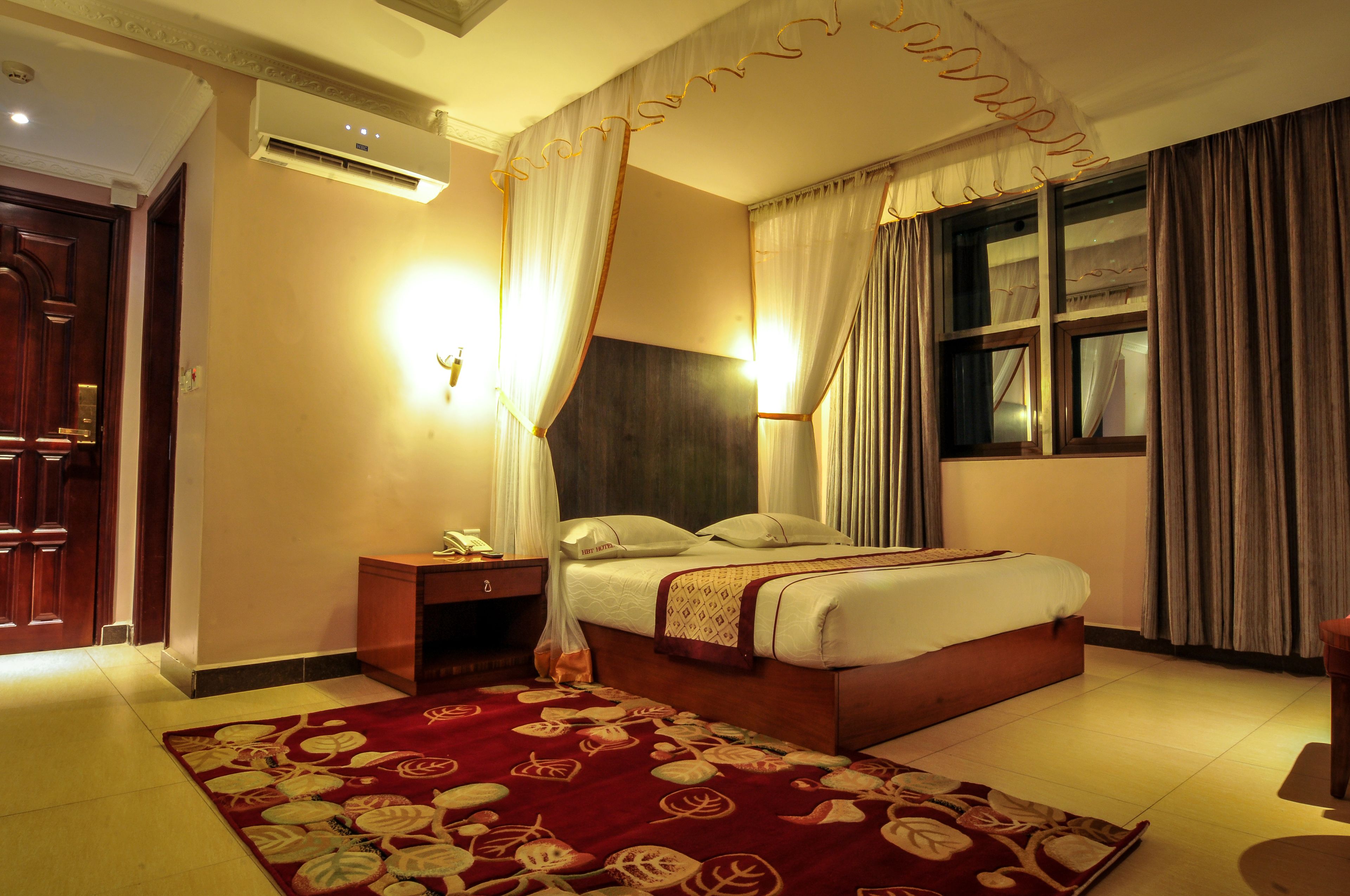 A hotel room with a bed, bedside table, and a window with curtains.