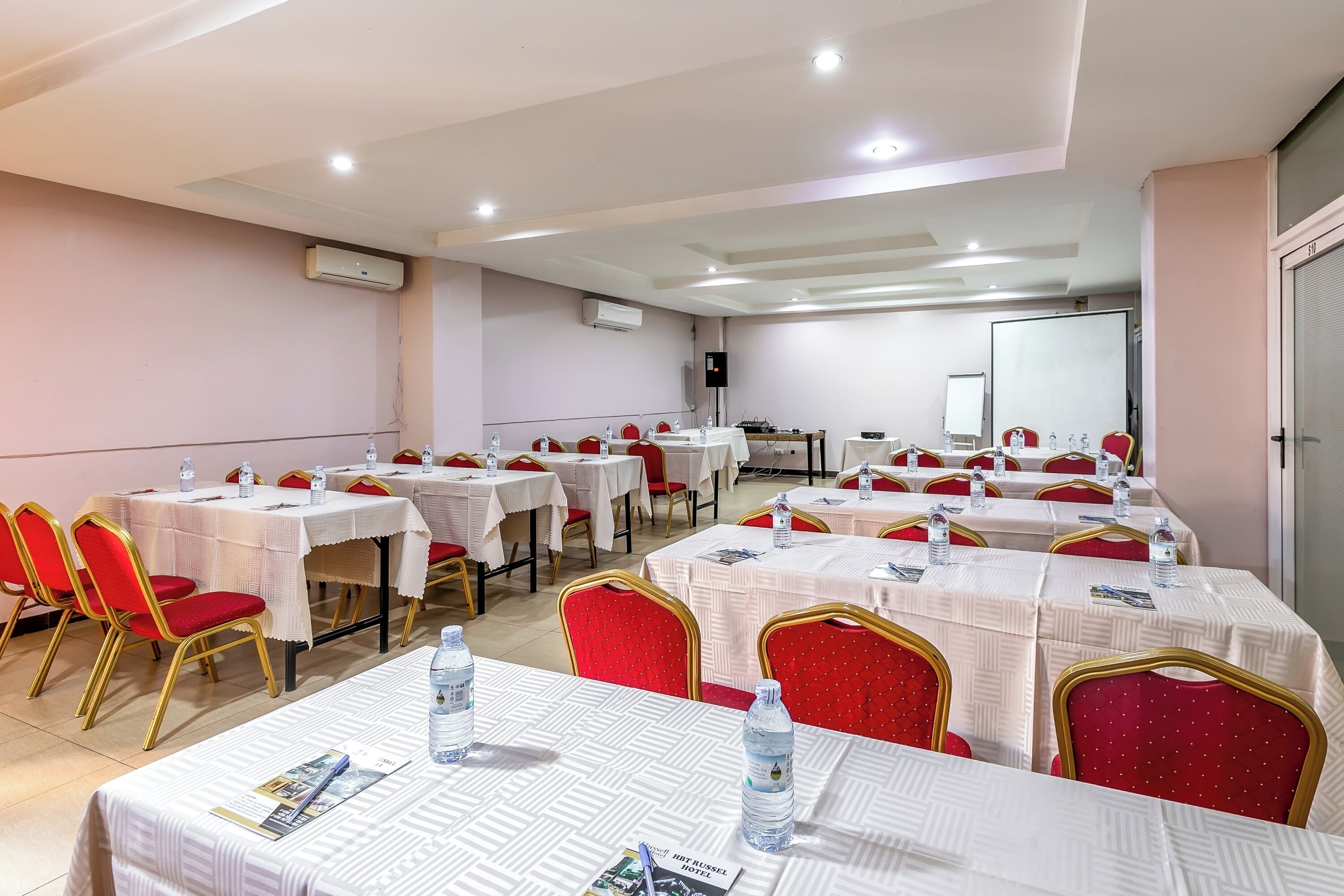 A conference room with multiple tables, red chairs, and white tablecloths.