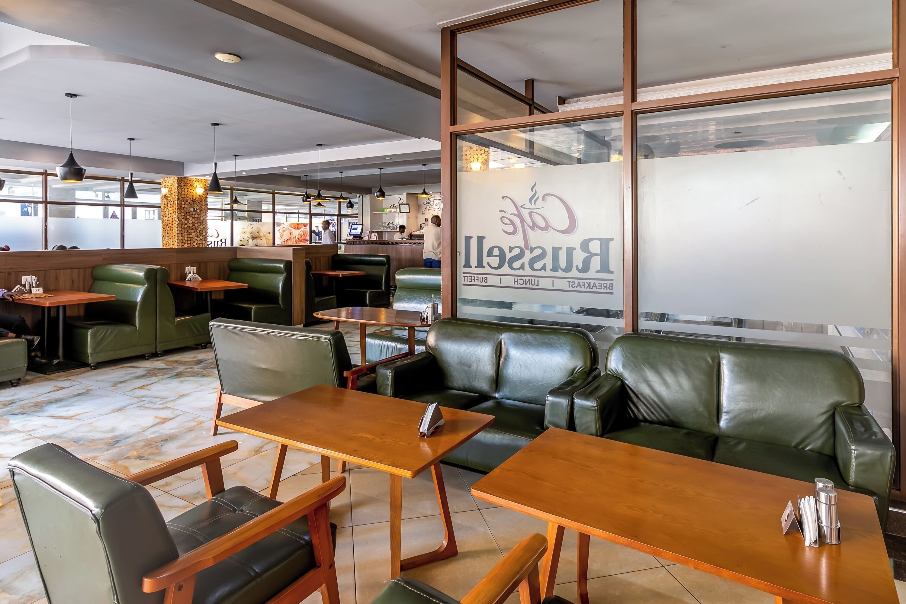 L'intérieur d'un restaurant est agrémenté de sièges en cuir vert, de tables en bois et de luminaires suspendus.
