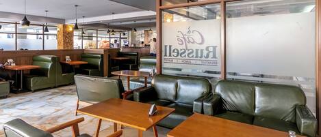 Een restaurantinterieur met groene leren zitplaatsen, houten tafels en hanglampen.