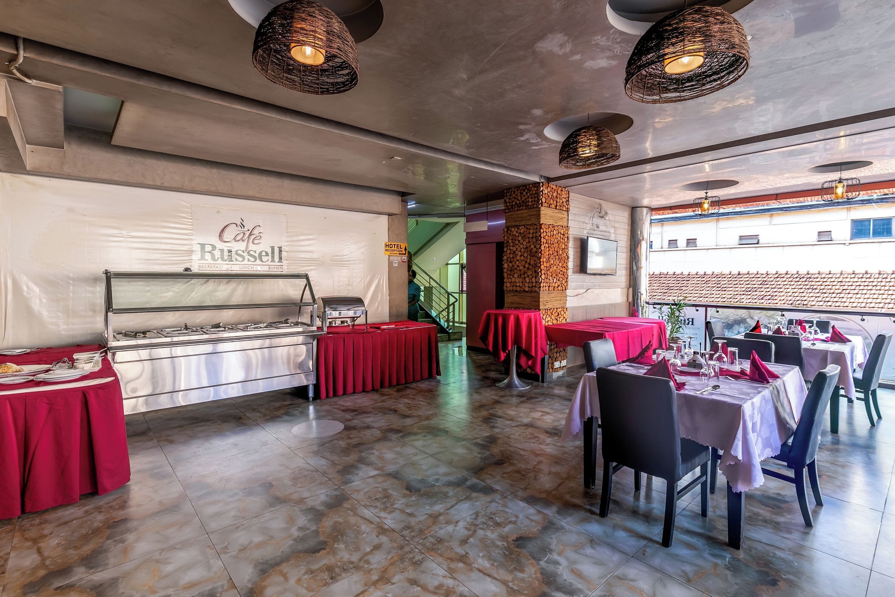 A restaurant with a buffet area, red tablecloths, and a staircase leading to an upper level.