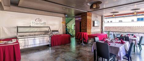 A restaurant with a buffet area, red tablecloths, and a staircase leading to an upper level.