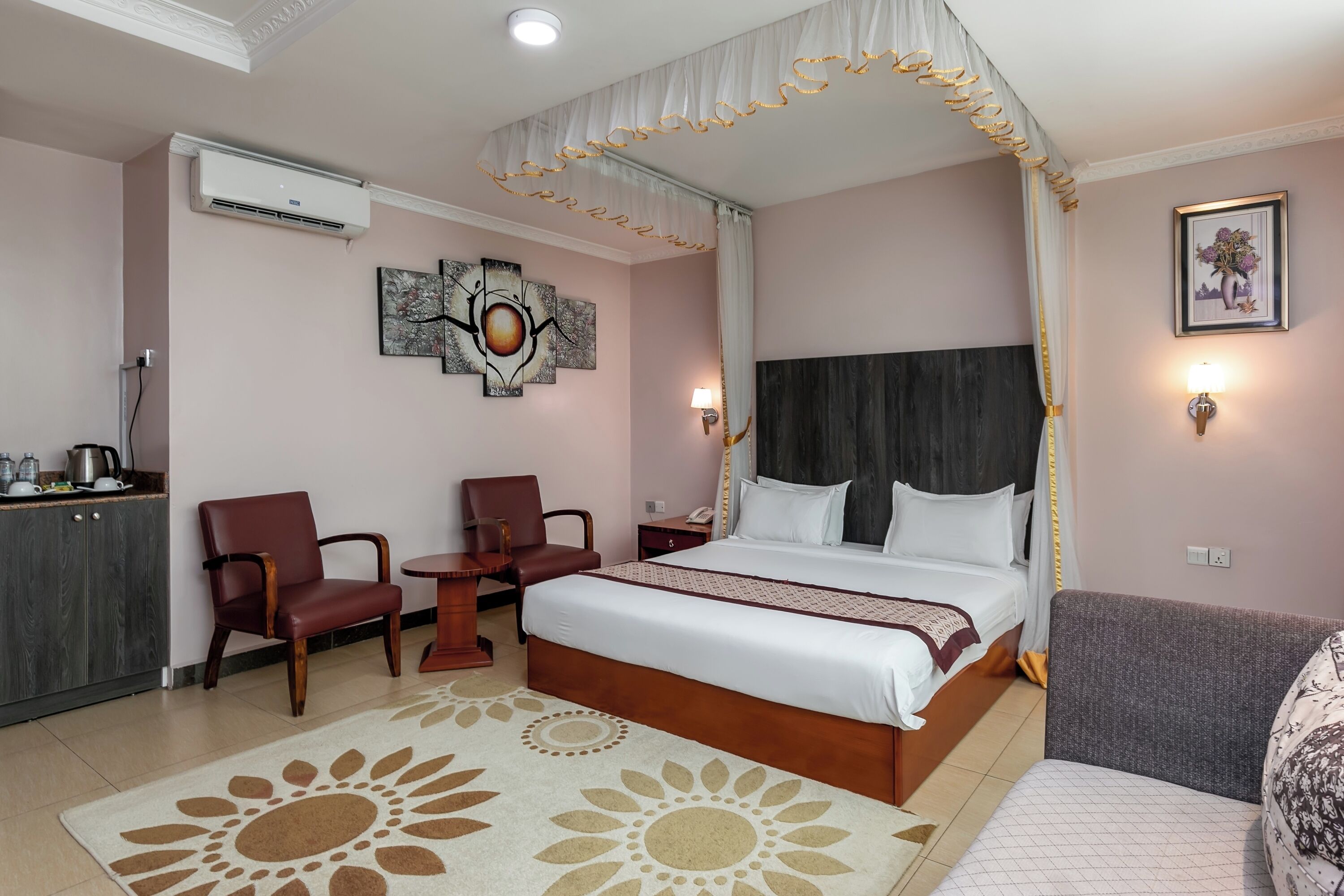 A hotel room with a large bed, a desk with a chair, a small table, and a sofa.