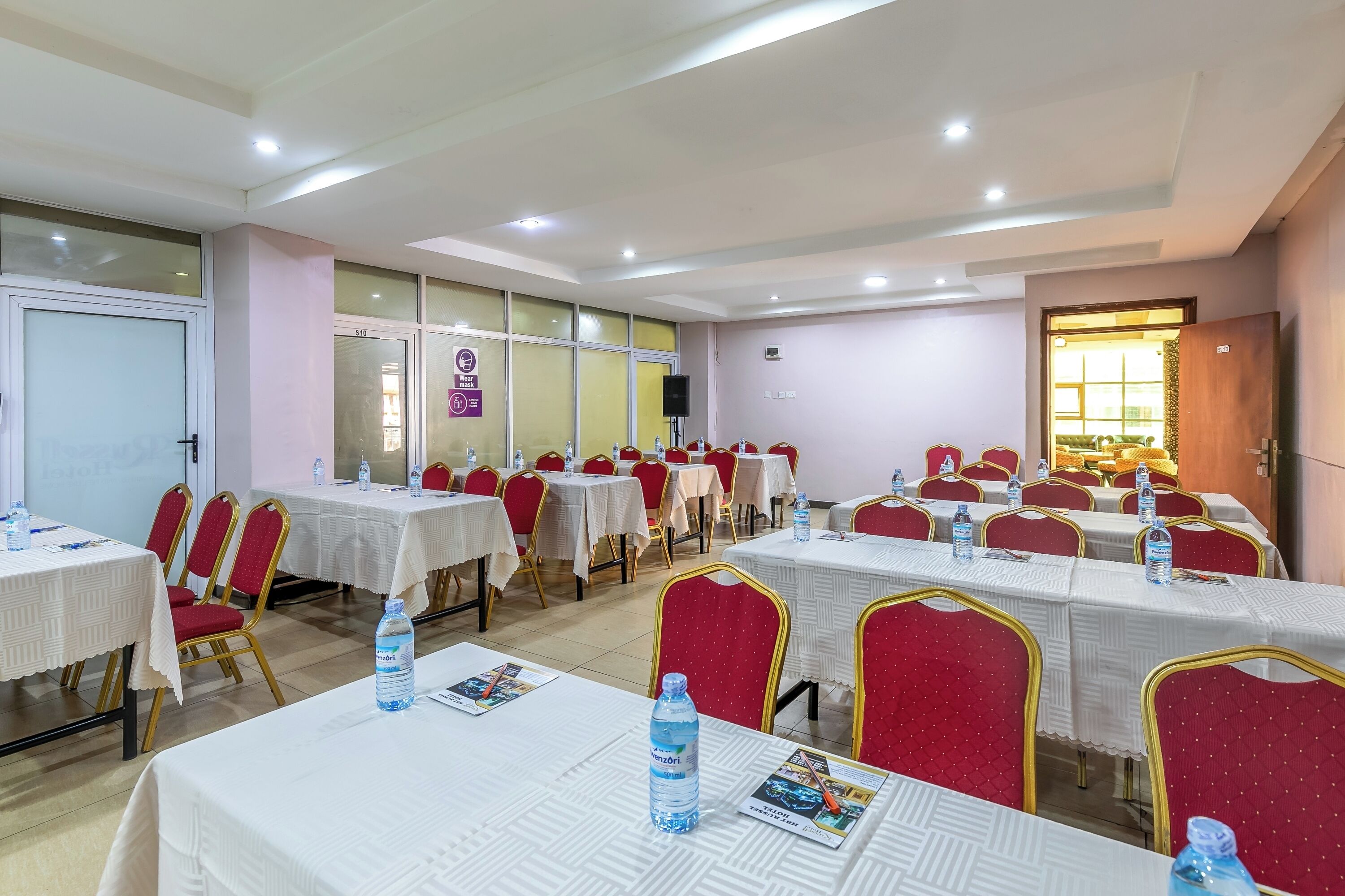 A conference room with multiple tables, red chairs, and white tablecloths.