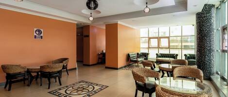 A hotel lobby with wicker furniture, a patterned rug, and a 'Wear mask' sign.