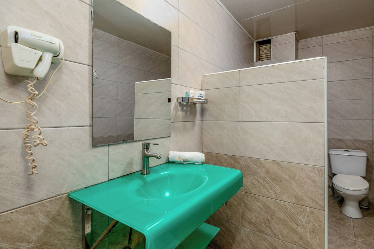 Un baño con un lavabo verde, un secador de pelo, un espejo, un dispensador de toallas y un inodoro.