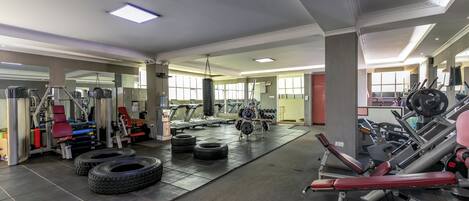 Un gimnasio con equipo de ejercicio, ventanas amplias y suelo de baldosas.