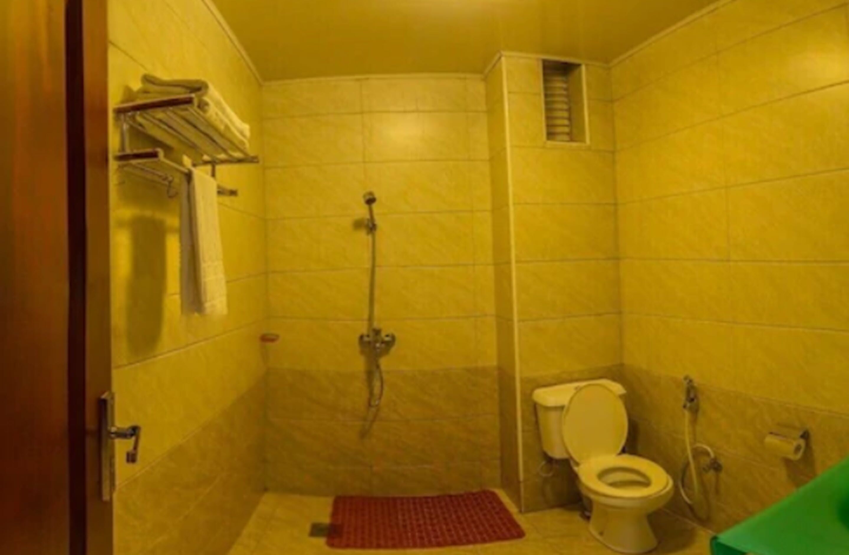 Un baño pequeño con azulejos amarillos, una ducha, un inodoro y un perchero para toallas.