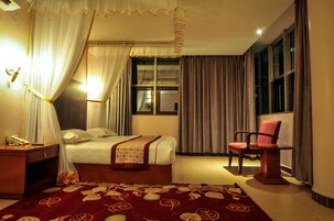A hotel room with a bed, a chair, a nightstand, and a window with curtains.