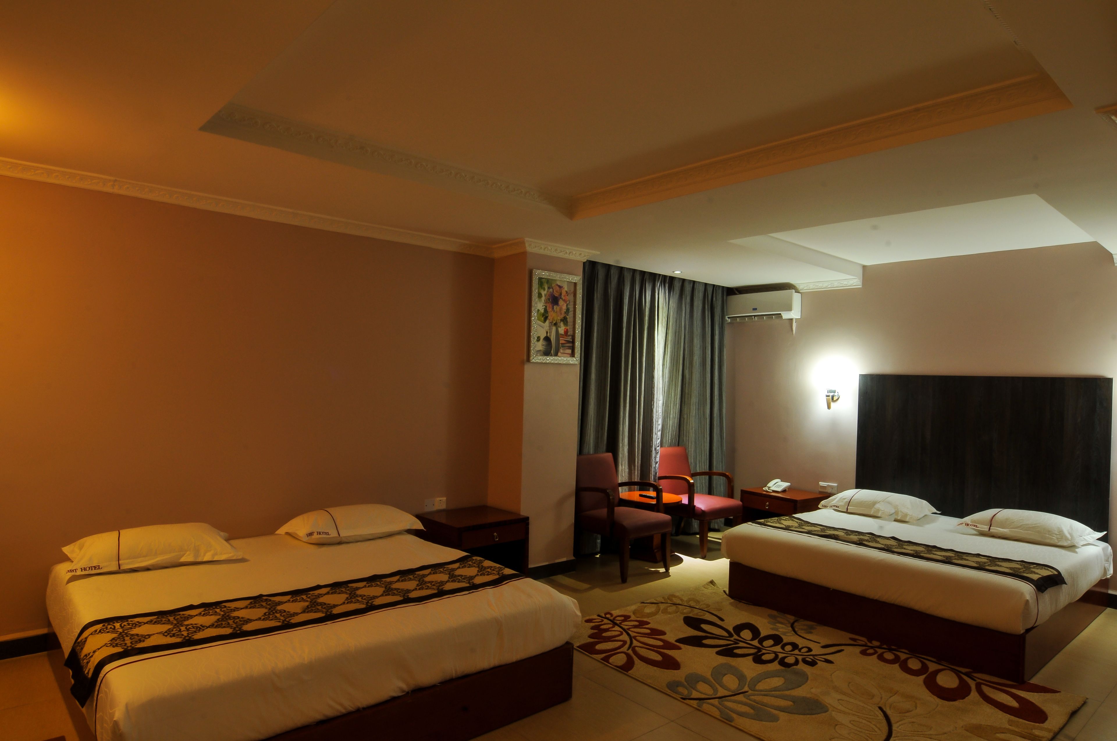 A hotel room with two beds, a desk, a chair, a nightstand, and a wall-mounted phone.