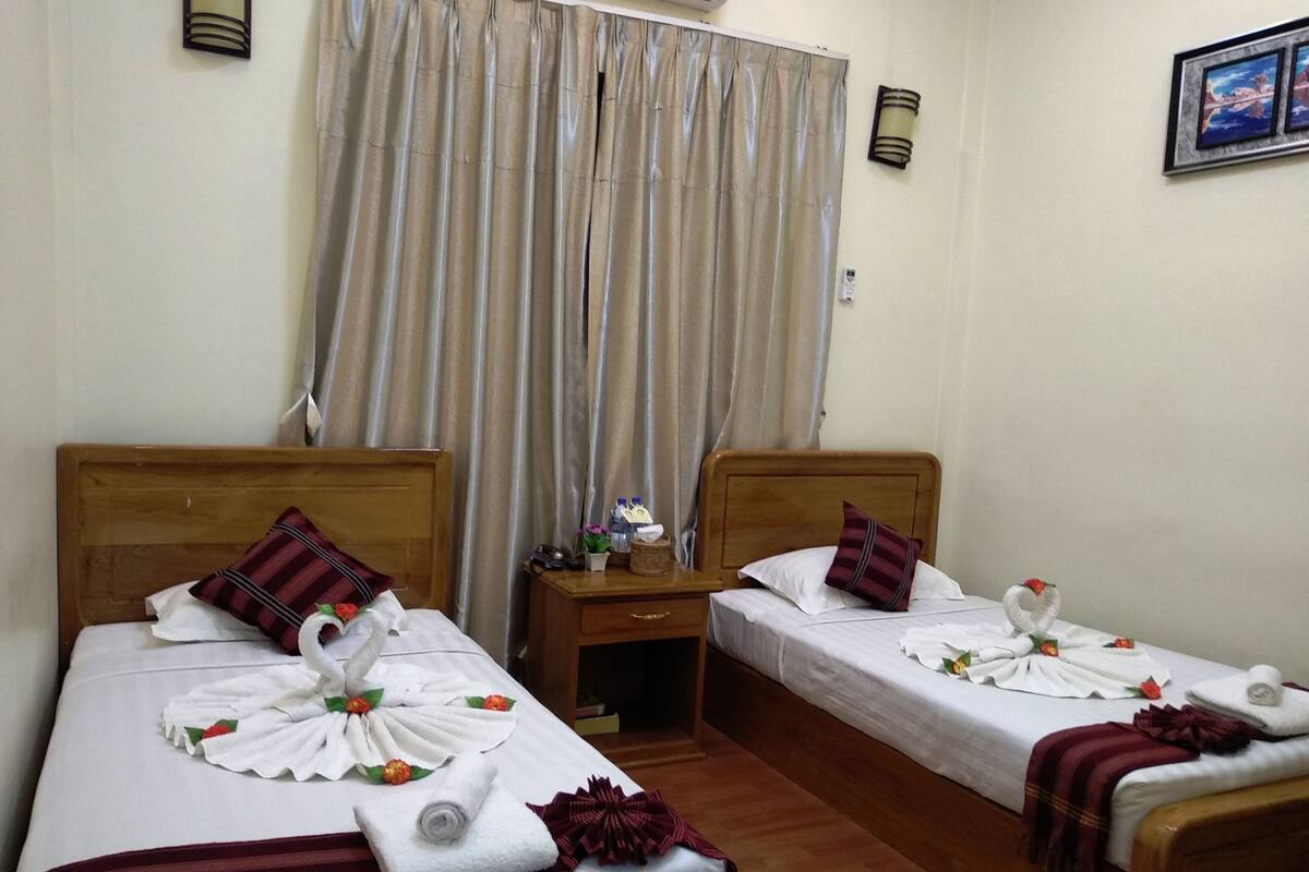 Een hotelkamer met twee eenpersoonsbedden, elk voorzien van handdoeken en kussens, een houten hoofdbord, een nachtkastje en een klein tafeltje met toiletartikelen.