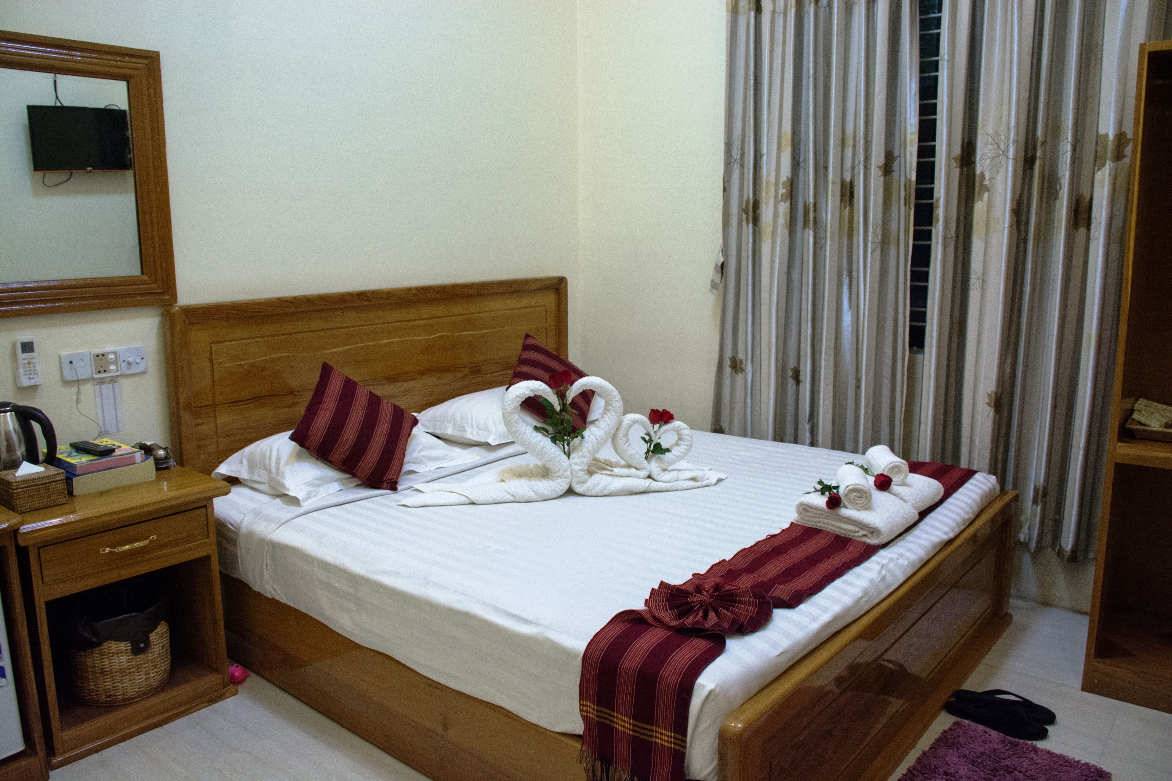 A neatly made bed with white linens, a wooden headboard, and decorative towels shaped like swans.