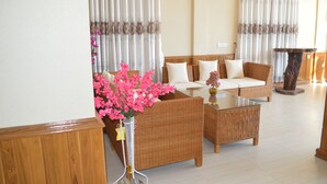Ein Wohnzimmer mit Korbmöbeln, einem Glastisch und einer Vase mit rosa Blumen.