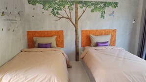 Een kamer met twee bedden, elk met hoofdeinde en kussen. Op de muur is een muurschildering van een boom met bladeren en vogels.