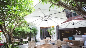 An outdoor seating area with tables and chairs, umbrellas, and greenery. - Sen Boutique Hotel (Da Nang)