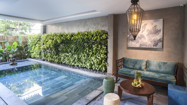 A modern indoor pool area with a green wall, a sofa, and a table with fruit. - Sen Boutique Hotel (Da Nang)