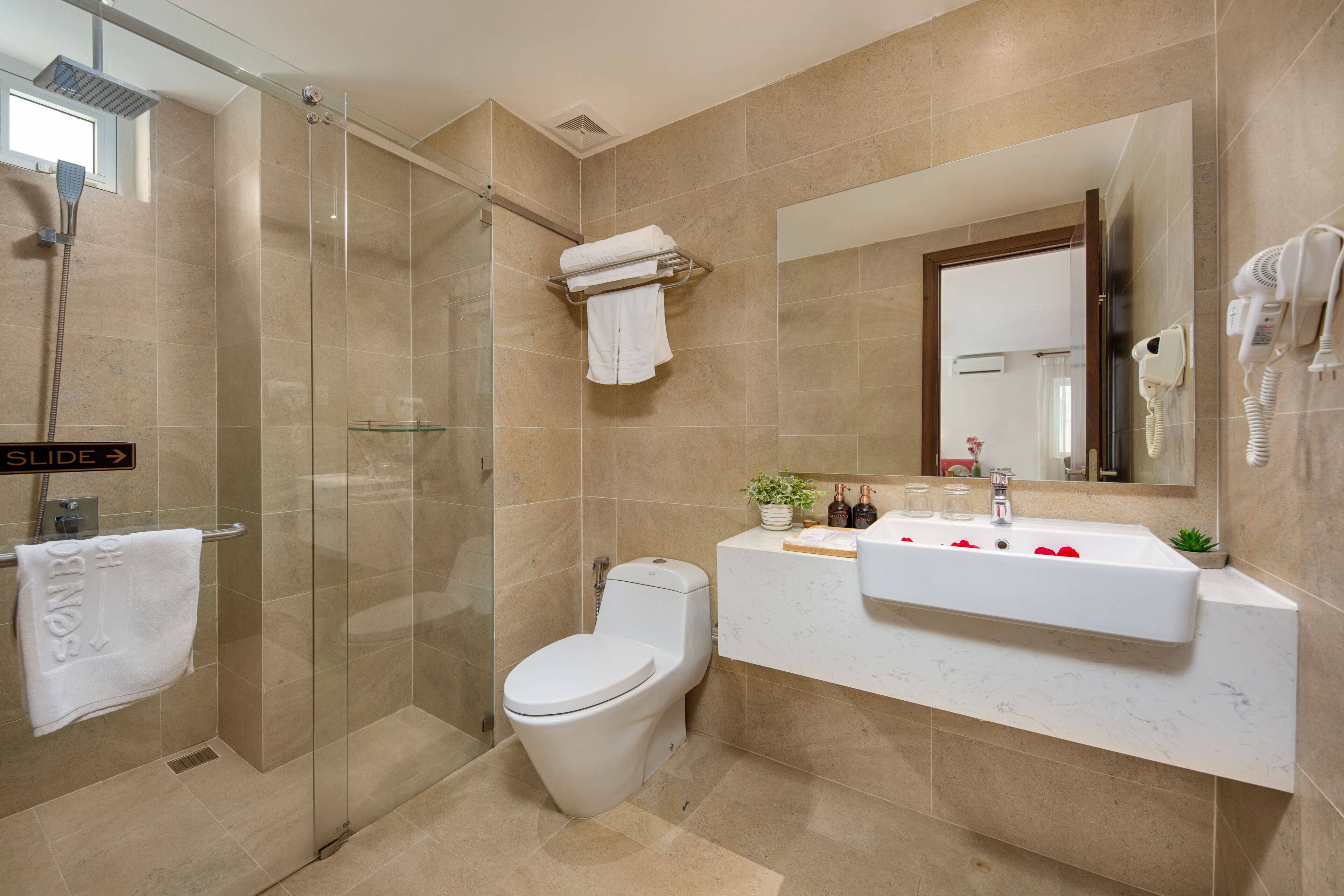Ein modernes Badezimmer mit einer Duschkabine, einer Toilette, einem Waschbecken mit Spiegel und einem an der Wand befestigten Fön.