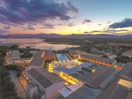 Un resort con diversi edifici, una piscina e vista su un lago e montagne.
