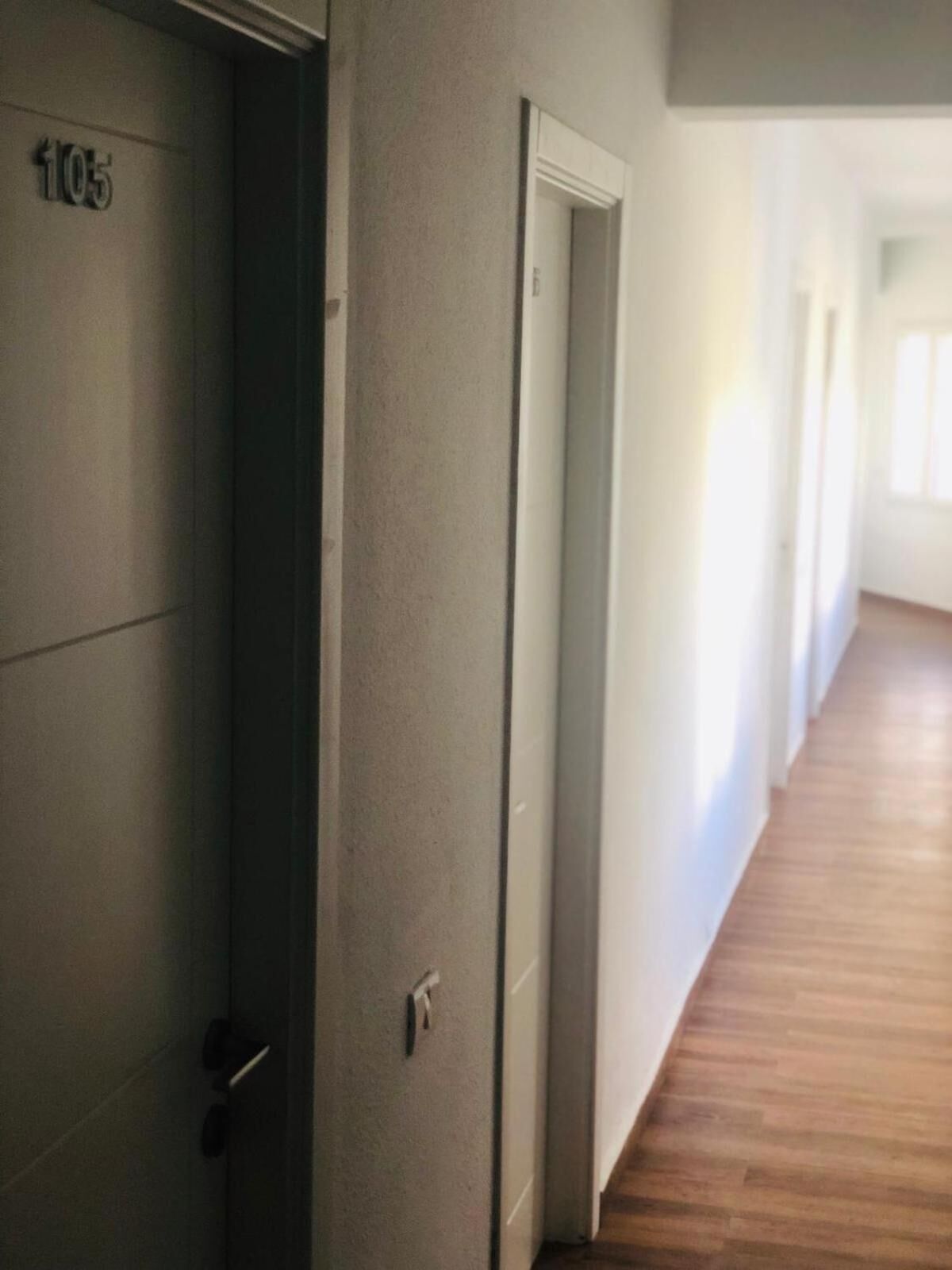 A corridor with a door labeled "105" leading to a room. The corridor has wooden flooring and white walls.
