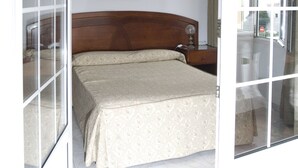 A bedroom with a bed, a nightstand, a framed picture on the wall, and a sliding glass door leading to a balcony. - Hotel Boomerang (Valverde)