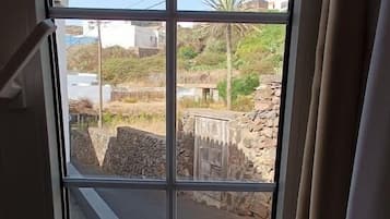 Habitación con un ventanal grande que da a una obra con muros de piedra y una palmera.