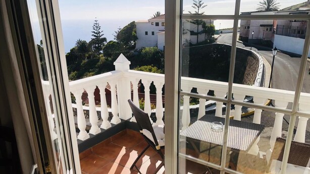 A balcony with a white balustrade, a tiled floor, and a table with a chair. - Hotel Boomerang (Valverde)