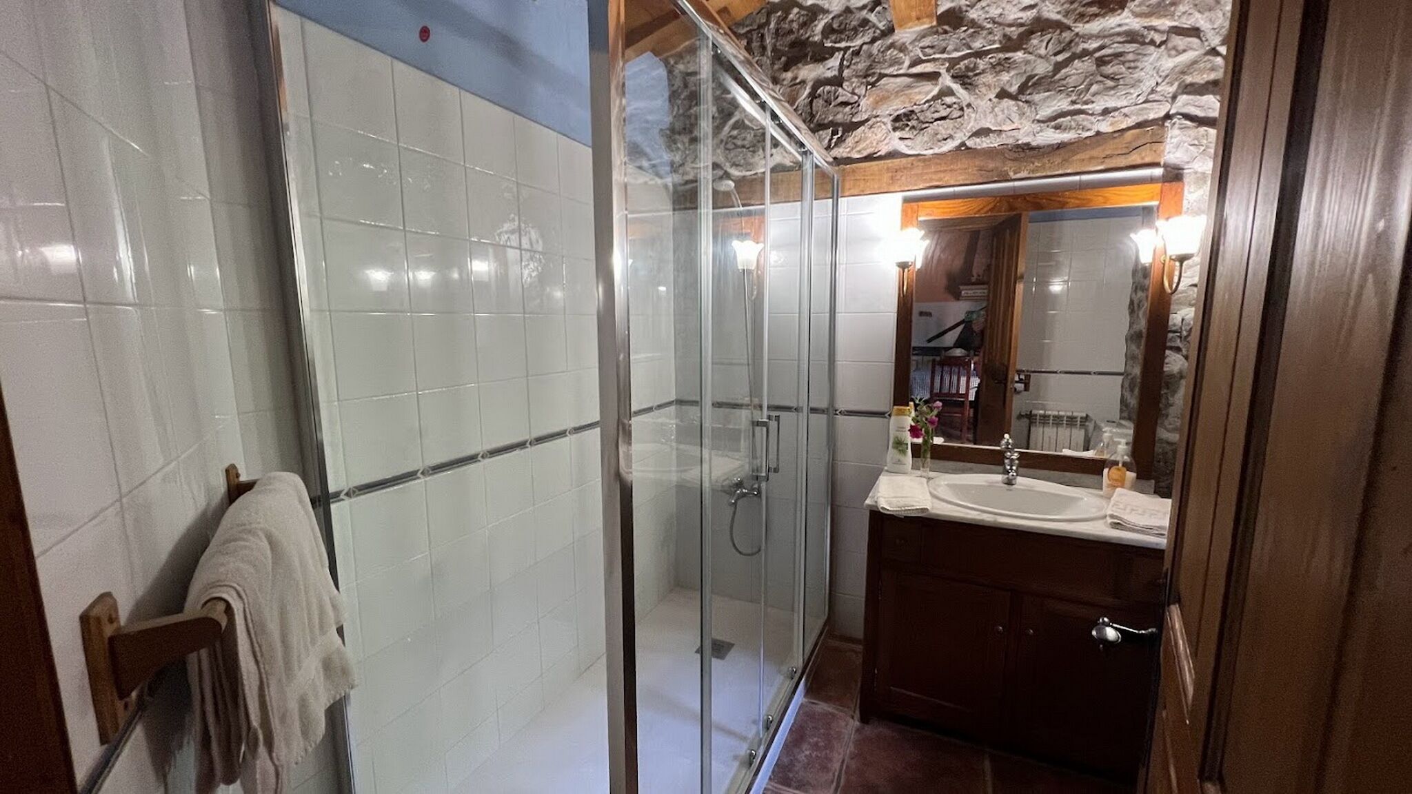 Un baño moderno con ducha envuelta en vidrio, tocador de madera con lavamanos y espejo sobre el tocador.