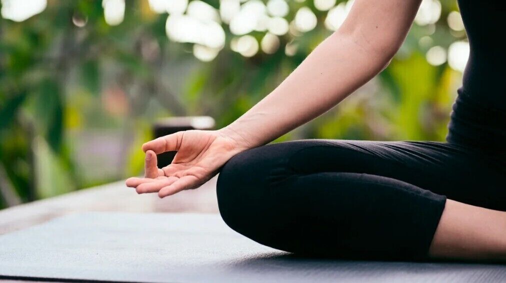 A person sitting on a yoga mat outdoors.