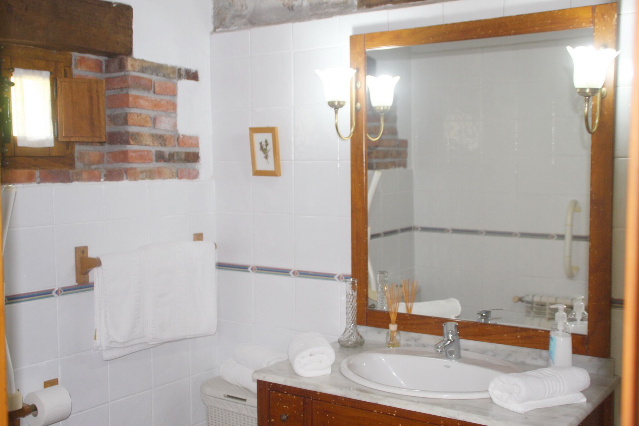 Een badkamer met een grote spiegel, witte tegels, een marmeren wastafel en een houten wastafelmeubel.