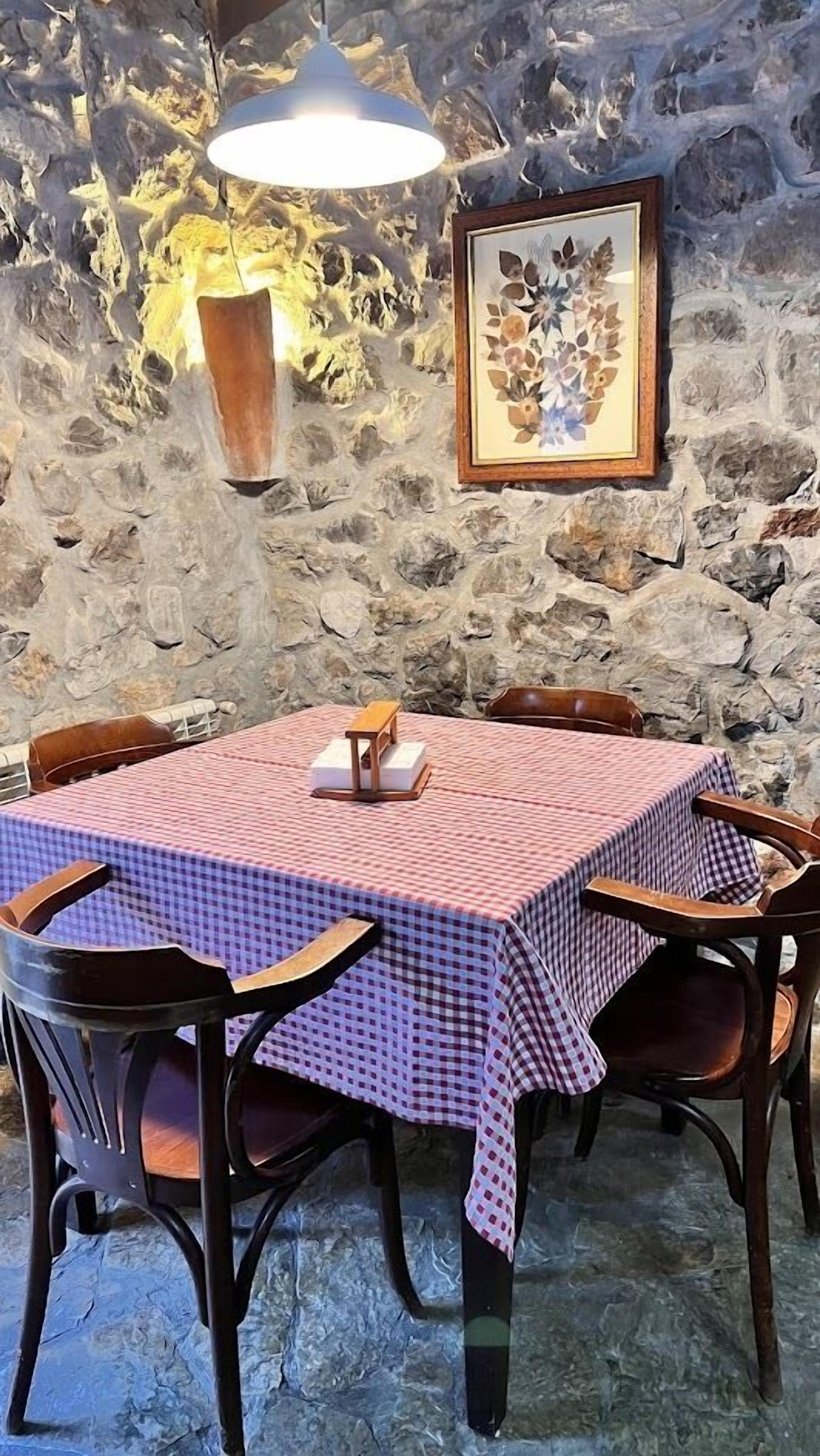 A stone wall with a framed floral artwork and a table with a checkered tablecloth.