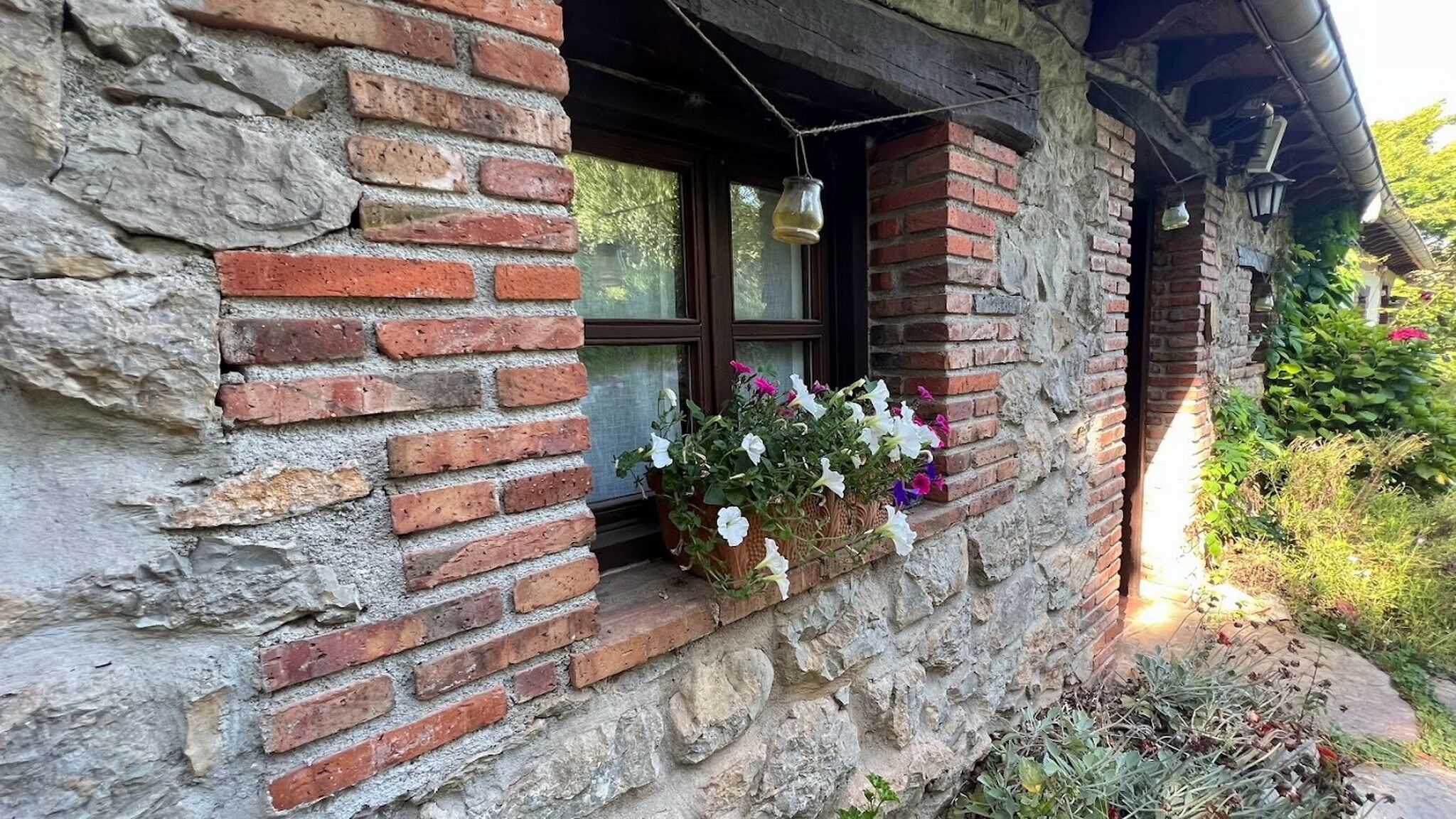 A rustic stone and brick building with a window featuring hanging flower baskets.