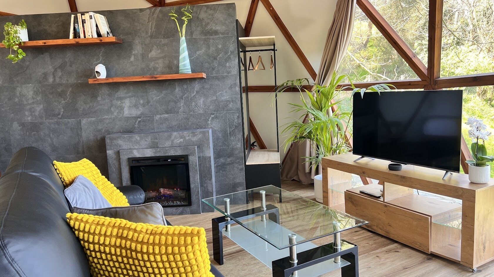 A modern living room with a fireplace, a sofa with yellow cushions, a glass coffee table, and a TV on a wooden stand.