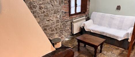 A cozy room with a stone wall, a white sofa, a wooden table, and a small candle on the floor.