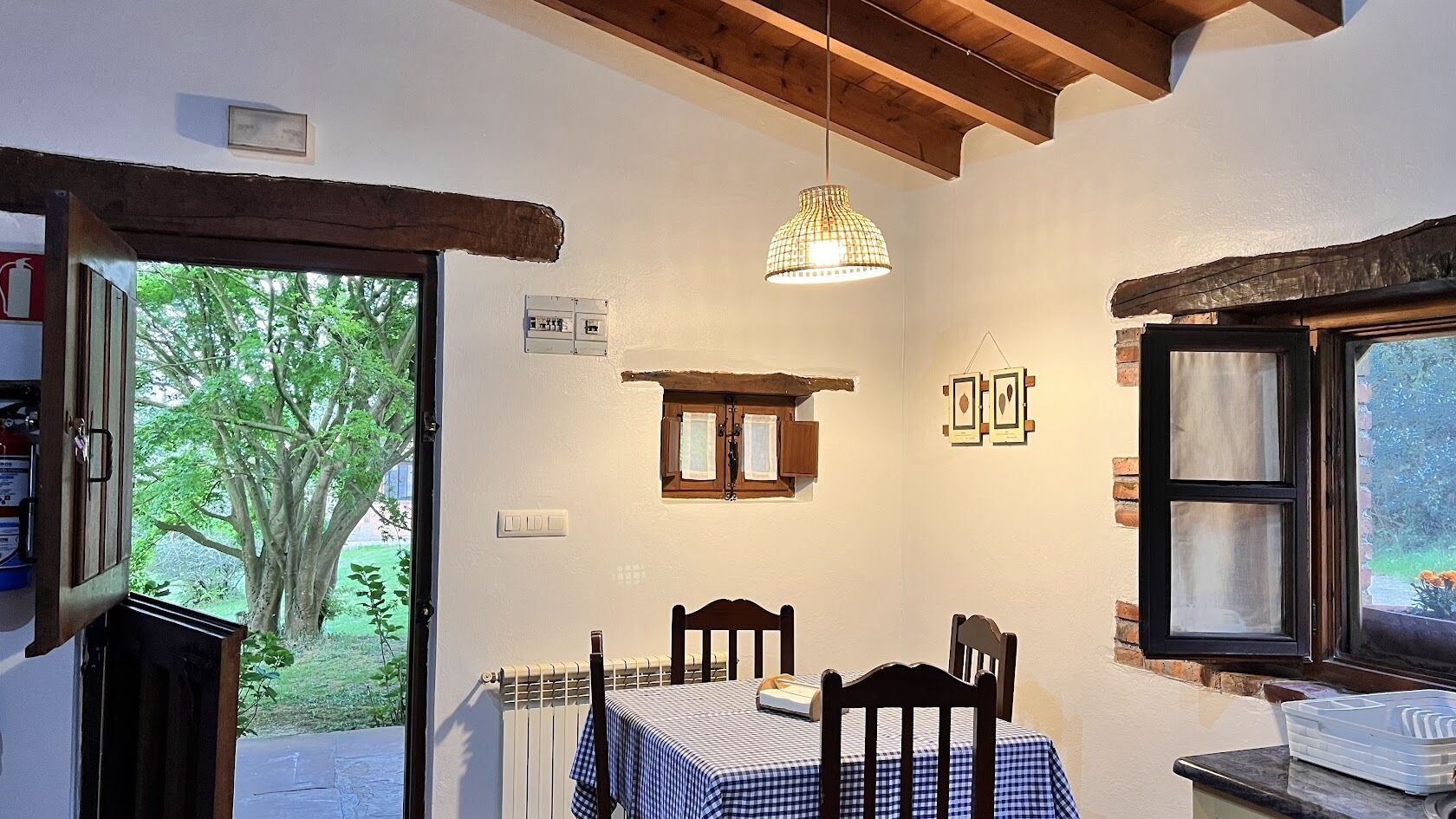 A cozy room with a table set for two, a hanging light fixture, and a window with a view of greenery.