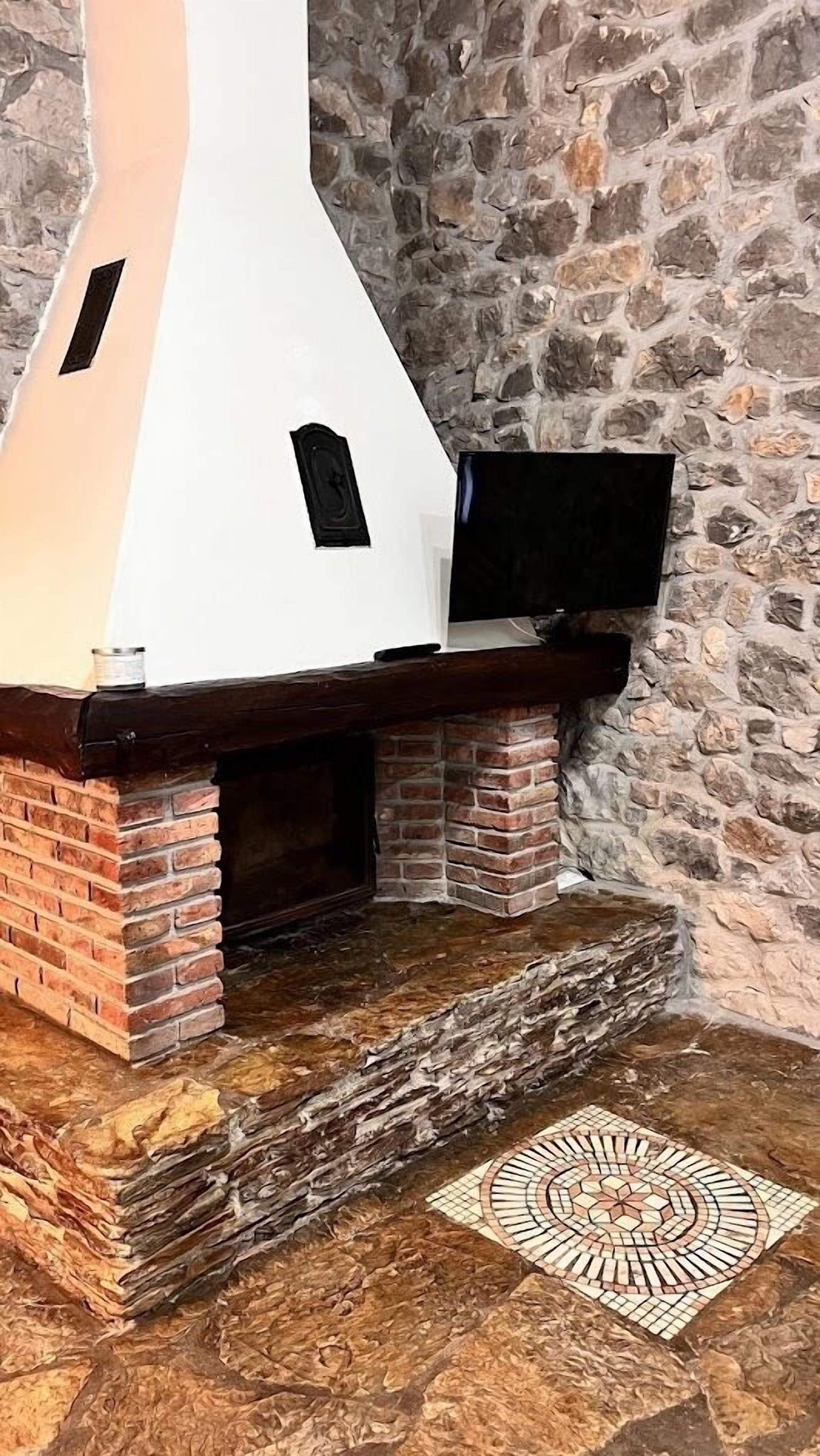 A stone wall with a fireplace featuring a TV on top.