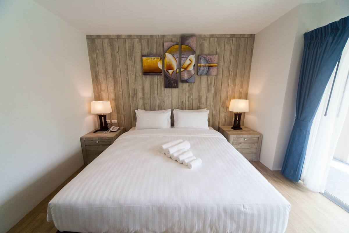 Una camera d'albergo con un letto grande, due comodini con lampade, una testiera di legno e una finestra con tende.