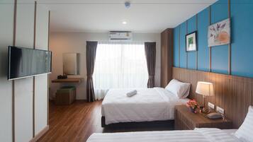A hotel room with two beds, a flat-screen TV, an air conditioning unit, a bedside table with a lamp and flowers, and a large window with curtains.