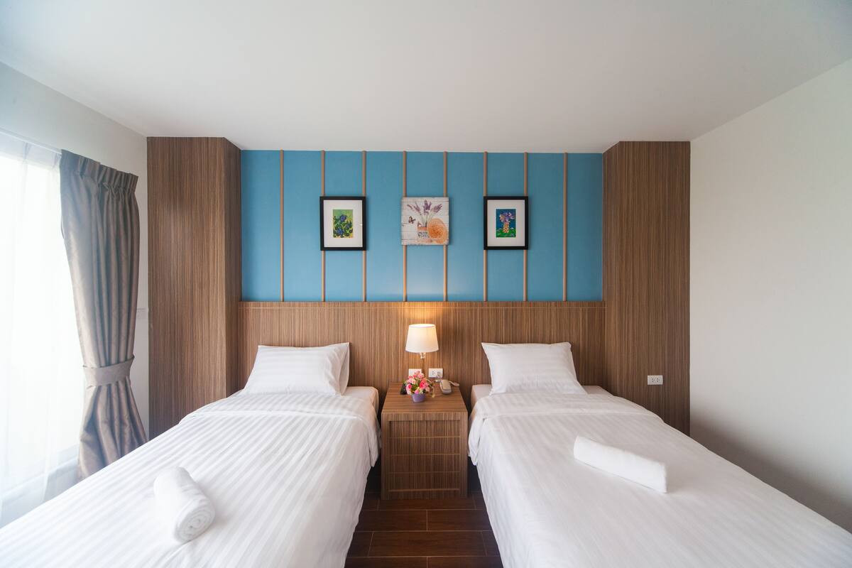 Una camera d'albergo con due letti, un comodino con una lampada e una parete decorata con quadri.